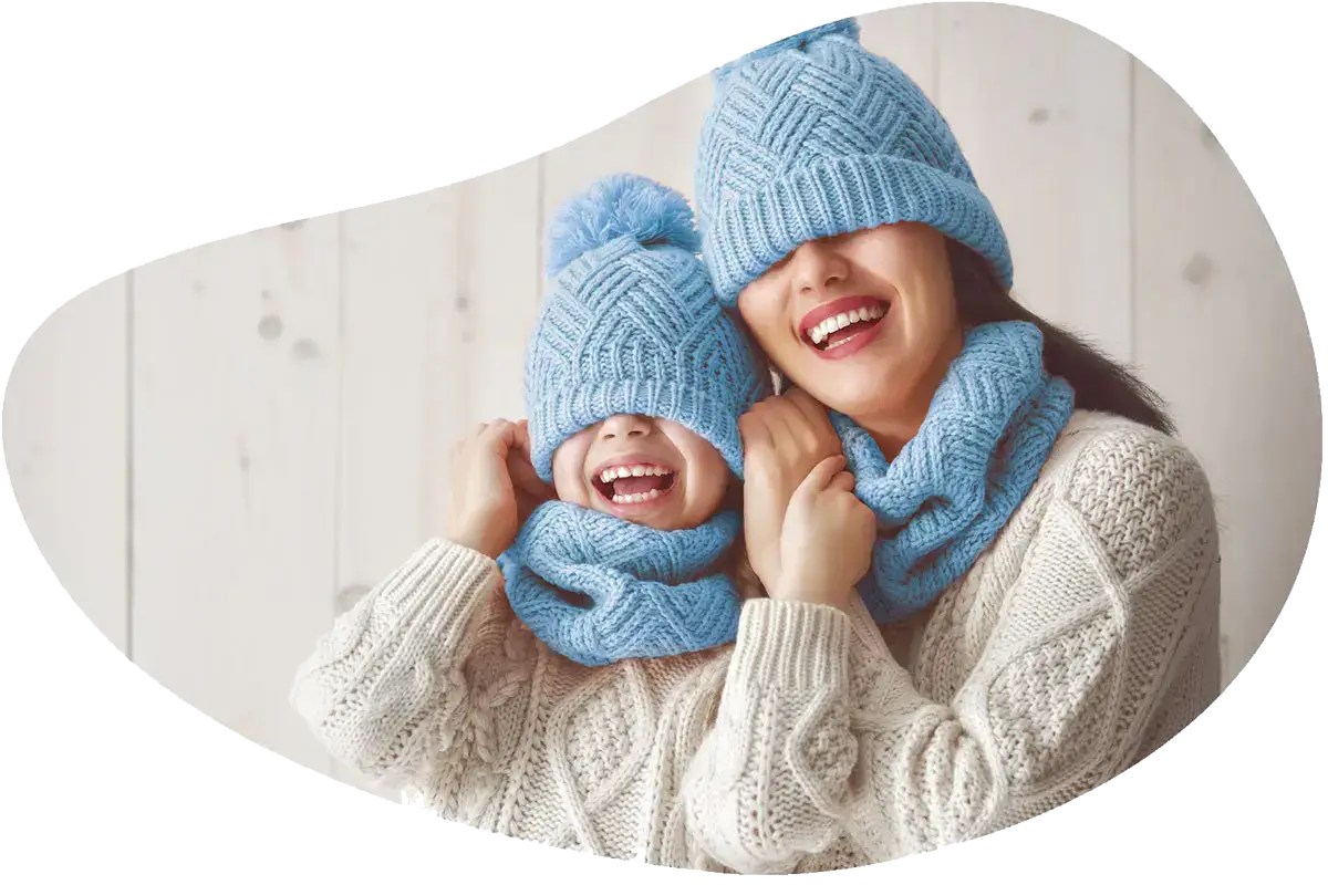 Mutter und Kind lachen mit tief ins Gesicht gezogenen Wintermützen und warmen Schals